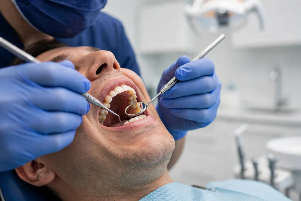 Dentist examining a patient's gums with a periodontal probe and dental mirror during a gum assessment